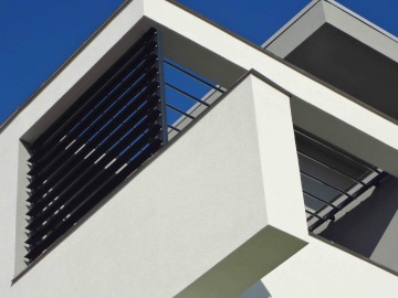 Moderní architektura s bílou fasádou a horizontálními kovovými lamelami na modré obloze.