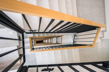 Pohled dolů na vnitřní schodiště administrativní budovy s vnitřním zábradlím.