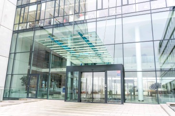 Vchod do moderní budovy Kavčí Hory s prosklenými stěnami a automatickými dveřmi.