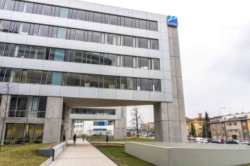 Moderní kancelářská budova Kavčí Hory s logem Net4Gas, lidé procházející po chodníku, městská zástavba v pozadí.