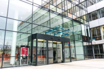 Skleněná fasáda moderní budovy Kavčí Hory s automatickými dveřmi a cyklistickým stojanem v popředí.