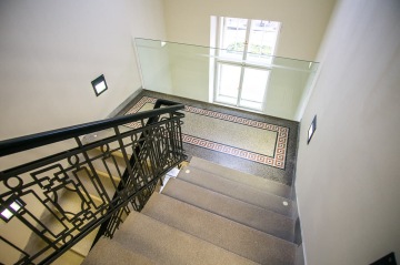 Schodiště se skleněným zábradlím a vzorovanou dlažbou u velkého okna.