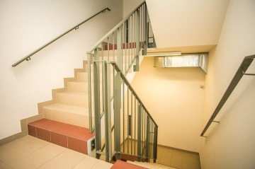 Schodiště s kovovým zábradlím a světlými dlaždicemi v interiéru.