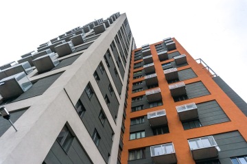 Moderní bytový dům s oranžovou a šedou fasádou, vyčnívající balkony.