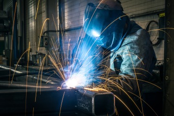 Svářeč v ochranné masce svařující ocelový rám, jiskry létající kolem.