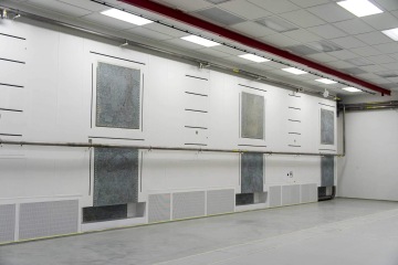 Velká místnost Laserové centrum ELI s bílými stěnami, kovovými potrubími a mřížkami, osvětlená stropními svítidly.