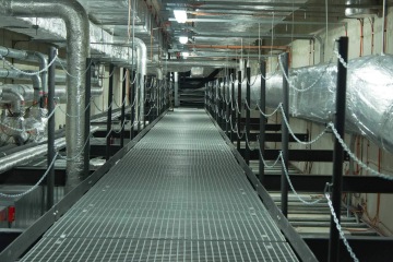 Chodba s technickými trubkami a drátěným zábradlím ve strojovně Laserové centrum ELI.