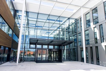 Moderní prosklený vstup do kancelářské budovy Laserové centrum ELI s bílými stínidly a zaparkovanými koly.