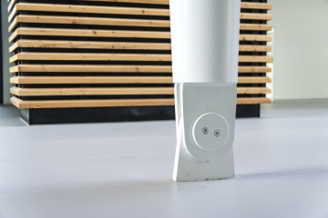 Bílý sloup s kulatým kováním v moderním interiéru, za ním dřevěná lamelová stěna.