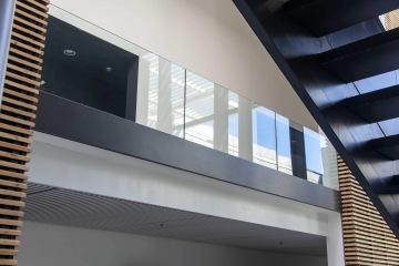 Moderní interiér Laserové centrum ELI s dřevěnými lamelami, skleněným zábradlím a černým schodištěm.