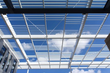 Moderní architektonická struktura Laserové centrum ELI s bílými lamelami proti modré obloze s obláčky.