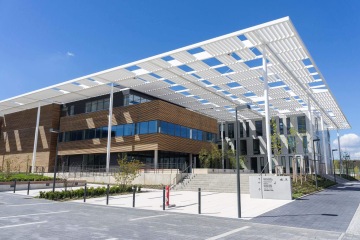 Moderní budova Laserové centrum ELI s bílou pergolou, dřevěným obložením a velkými okny na jasné obloze.