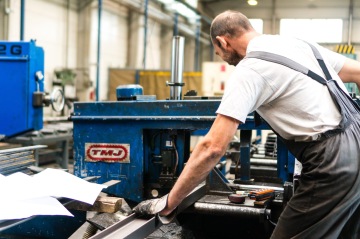 Pracovník v montérkách obsluhuje průmyslový stroj v továrně.