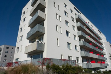 Moderní bytový dům BD Zahrady Opatov s několika balkony, bílou fasádou a šedými balkonovými zábradlími za slunečného dne.