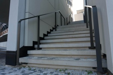 Moderní venkovní schodiště s kovovými zábradlími mezi dvěma budovami BD 4U Living.