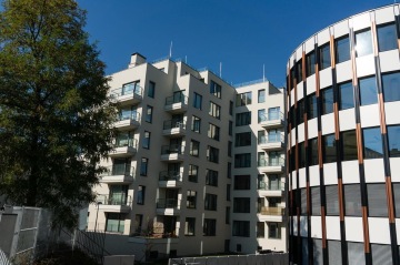 Moderní bytový dům BD 4U Living se skleněnými balkony a vedlejší zaoblenou budovou na modré obloze.