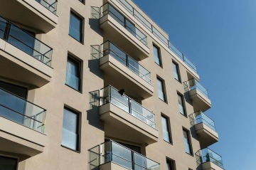 Moderní bytový dům BD 4U Living s prosklenými balkony na modré obloze.