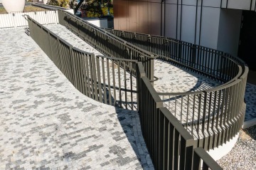 Zakřivená rampa s kovovým zábradlím na dlážděném povrchu u moderní budovy BD 4U Living.