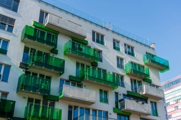 Bytový dům Tesla Vršovice s balkony z tmavě zeleného skla proti modré obloze.