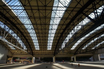Velká průmyslová hala s ocelovou konstrukcí a skleněnou střechou, osvětlená přirozeným světlem.