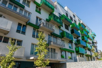 Moderní bytový dům Tesla Vršovice s balkony a zelenými skleněnými zábradlími, slunečný den.