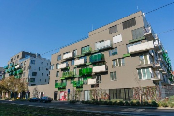 Moderní bytový dům Tesla Vršovice s barevnými balkony a parkem in front of building pod modrou oblohou.