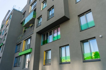 Moderní obytná budova Tesla Vršovice s barevnými skleněnými balkonovými zábradlími a bezpečnostní kamerou.