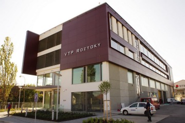 Moderní kancelářská budova VTP Roztoky s auty zaparkovanými před ní za slunečného dne.