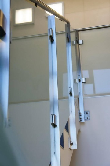 Vnitřní skleněné zábradlí s nerezovými madly na schodišti.