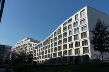 Moderní bytový dům BD Port Karolína, Praha s balkonem, modrá obloha a stromy v popředí.