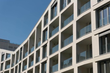 Moderní bytový dům BD Port Karolína, Praha s balkonovými zábradlími ze skla na modré obloze.