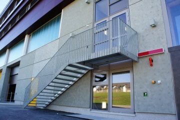 Vnější moderní kovové schodiště vedoucí k východu na patře průmyslové budovy.