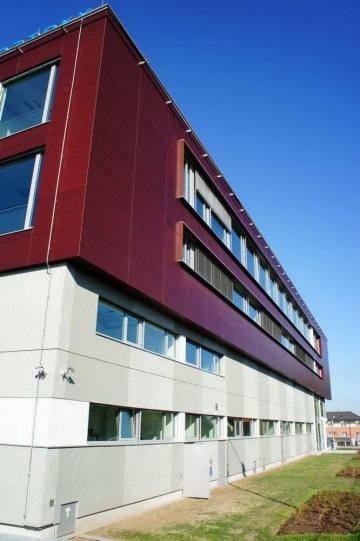 Moderní budova VTP Roztoky s červenou fasádou a velkými okny pod modrou oblohou.