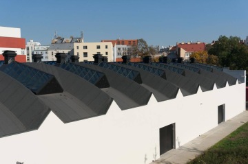 Střecha budovy Palmovka Open Park O s řadou moderních světlíků v městské čtvrti, na pozadí budovy a stromy.