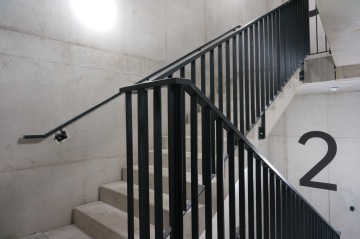 Betonové schodiště s kovovým zábradlím a černým číslem dvě na zdi.