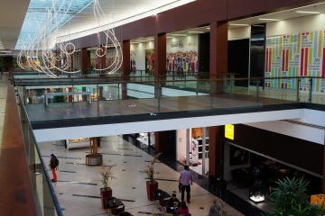 Nákupní centrum Galerie Harfa s prosklenými zábradlími a zavěšenými dekoracemi. Lidé procházejí kolem obchodů.