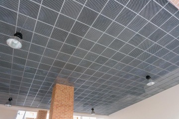 Stropní podhled z kovové mříže s zavěšenými lampami, cihlový sloup.