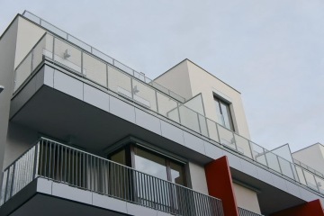 Moderní bytový dům s venkovním zábradlím balkonů a teras s příčkovými výplněmi.