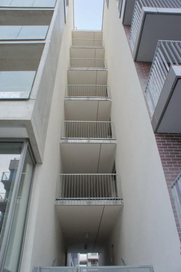 Moderní bytový dům s venkovním kovovým zábradlím balkonů.