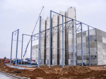 Stavební jeřáb sestavuje kovovou konstrukci Kimberly Clark Jaroměř kolem sila a budovy na staveništi.