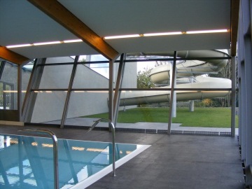 Vnitřní bazén se skluzavkou viditelnou přes velká okna, moderní architektura.