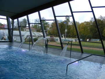 Vnitřní bazén s fontánami a výhledem na venkovní zahradu a trávník.