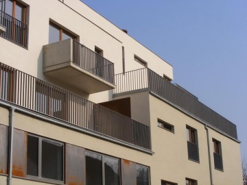 Moderní bytový dům Pod Tyršovým vrchem s balkony a minimalistickou architekturou na jasné obloze.