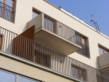 Moderní bytový dům Pod Tyršovým vrchem s balkóny a kovovým zábradlím pod modrou oblohou.