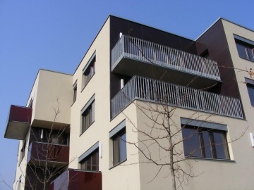 Moderní bytový dům Mazanka s balkony a bezlistý strom pod modrou oblohou.