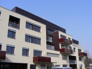 Moderní bytový dům Mazanka s balkony a velkými okny za slunečného dne.