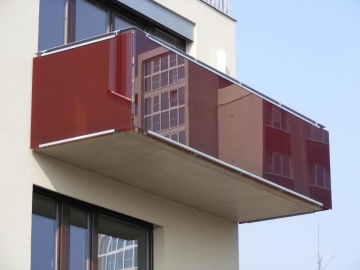 Bytový balkon s tmavě červeným skleněným zábradlím, odrážející okolní budovu Mazanka.