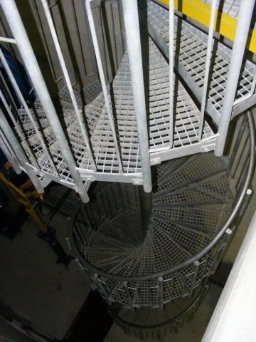 Kovové točité schodiště s rošty a zábradlím.