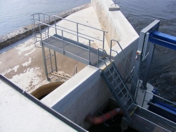 Průmyslová konstrukce s kovovým schodištěm a zábradlím vedle vodní elektrárny.