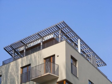 Moderní budova Pod Tyršovým vrchem s terasou na střeše, modrá obloha v pozadí.